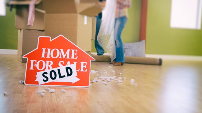 Moving:,Couple,Packing,With,Sold,Sign,In,Foreground