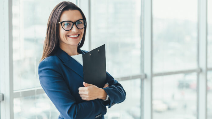 Confident,Young,Businesswoman,Standing,With,Folder,In,Hands,,Looking,At