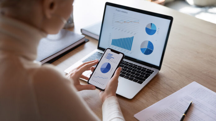 Woman,Hold,Smartphone,Use,Pc,At,Workplace.,Project,Stats,Financial