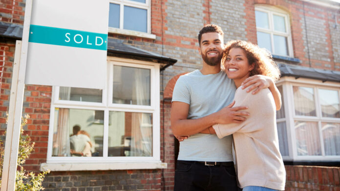 Portrait,Of,Excited,Couple,Standing,Outside,New,Home,With,Sold