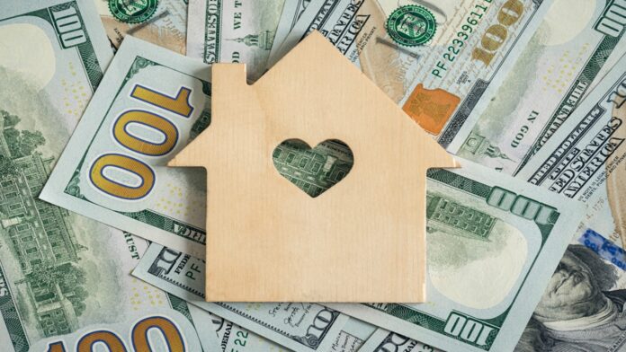 Wooden,House,Model,On,Background,Of,Us,Dollars,Banknotes.,Housing